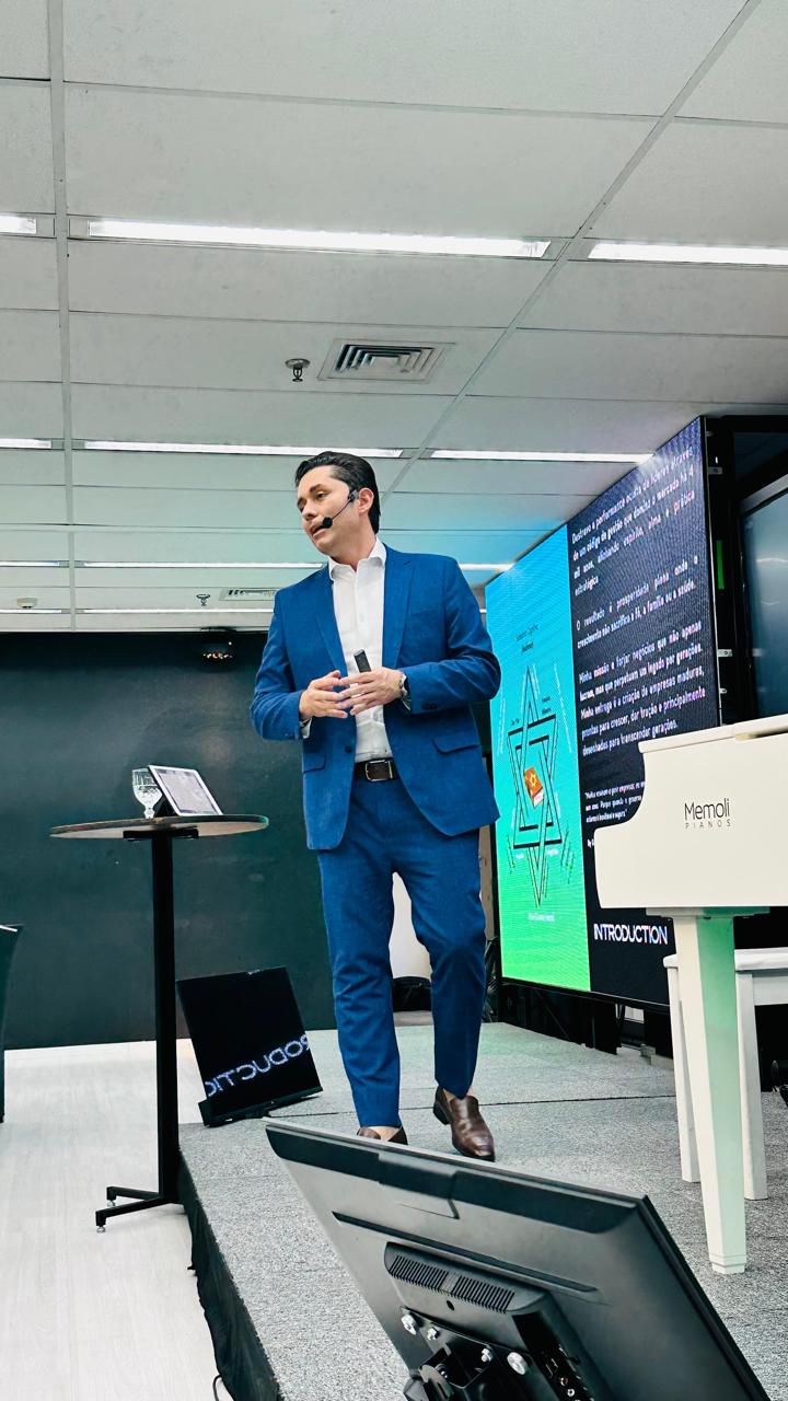 Gustavo Coelho caminhando em sala de estúdio, próximo a um piano de cauda branco
